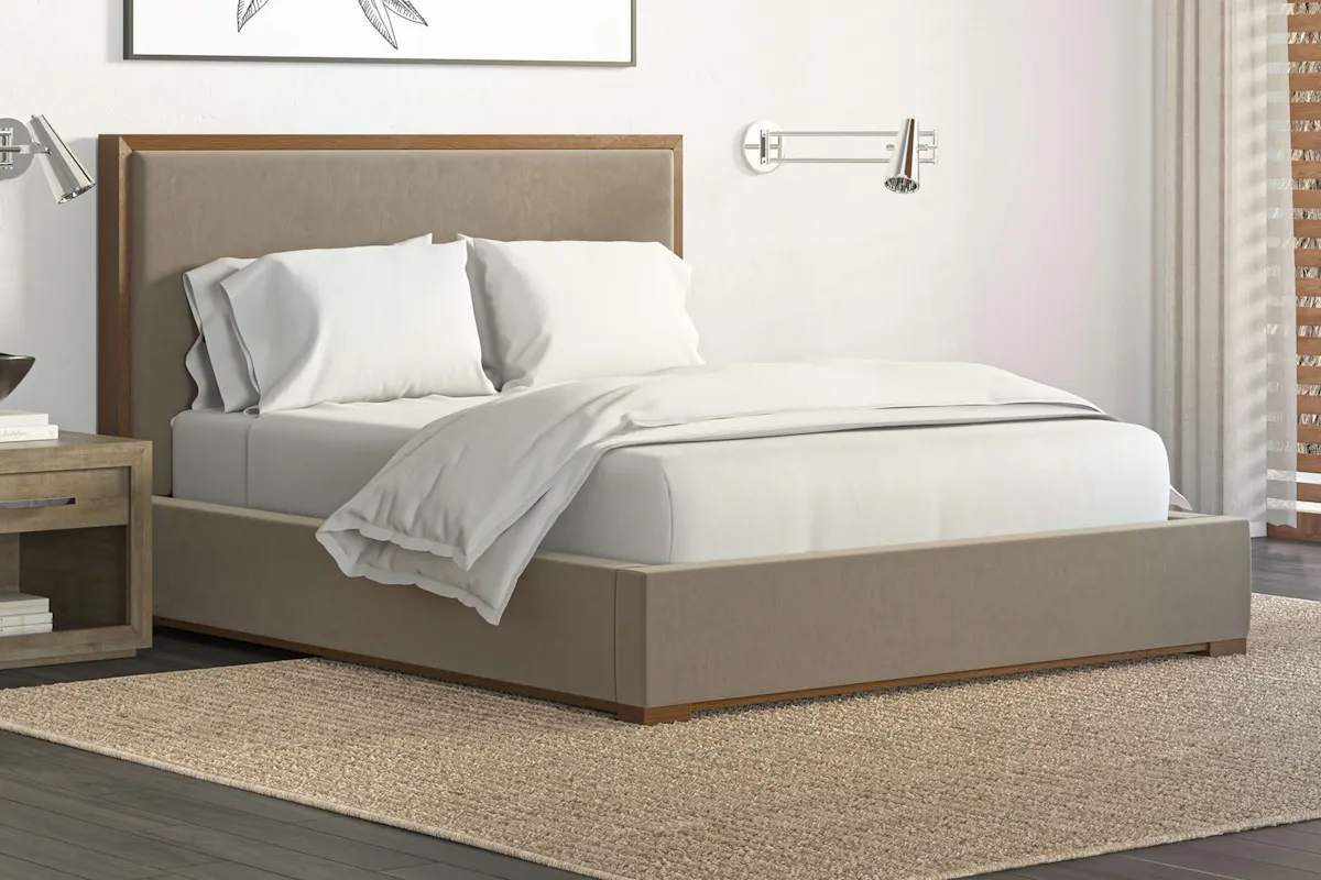 Saatva Lyon platform bed frame in taupe linen, room angle view showing substantial footboard and upholstered side rails